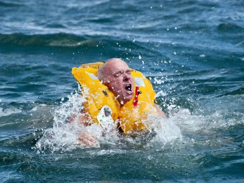 Muž v záchranné vestě po pádu do studené vody lapá po dechu.
