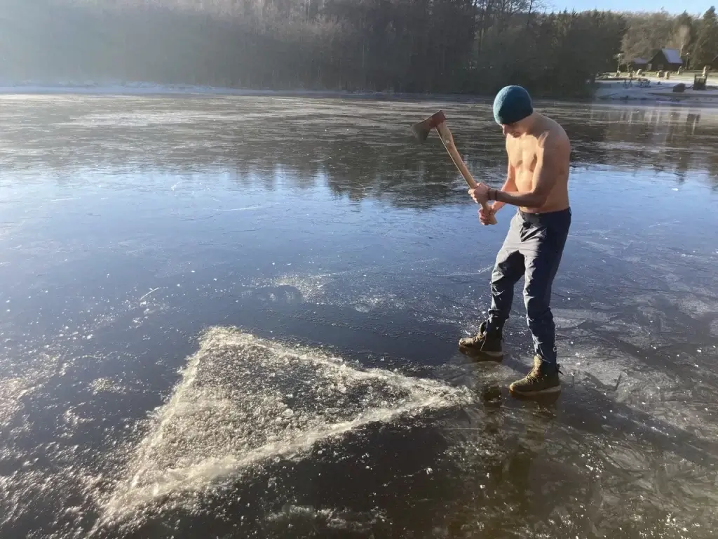 otužilec seká led na zamrzlém rybníce